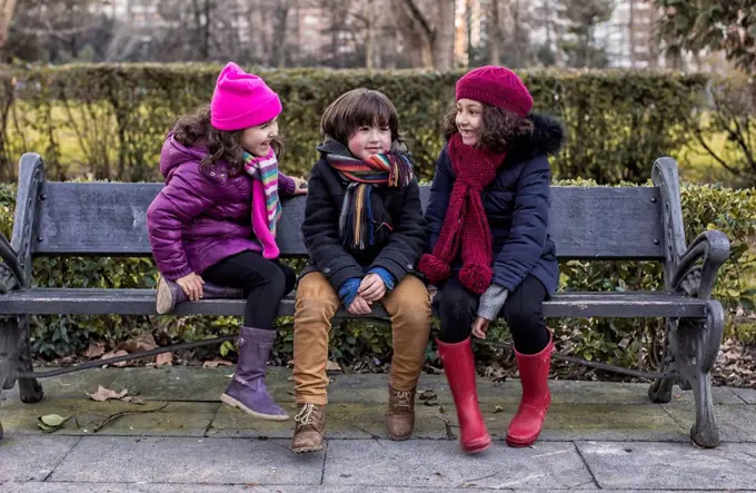 Three childrensitting on bench in a park on a winter day