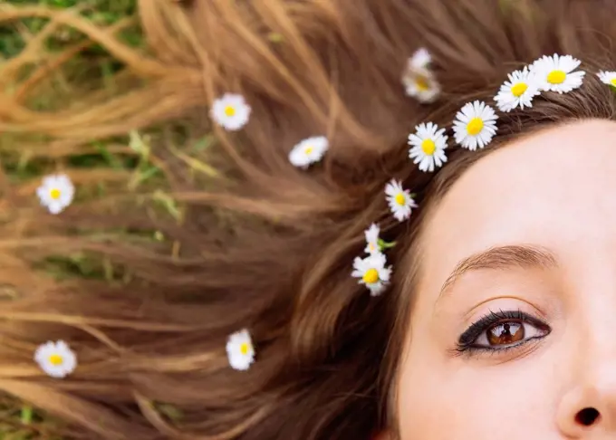 Woman lying on a meadow wearing daisies in her hair, close-up