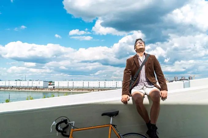 Mature man with bicycle sitting on wall enjoying weather