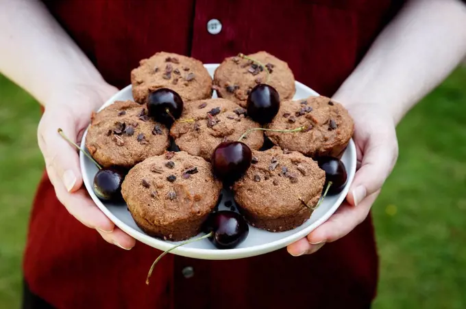 Man holding plate with vegan chocolate muffins with cherries