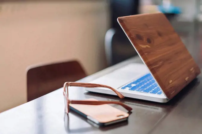 Wooden laptop, smartphone and glasses on desk