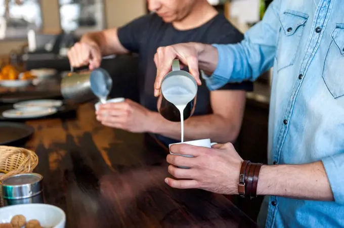 Two men preparing coffee with milk in a cafe