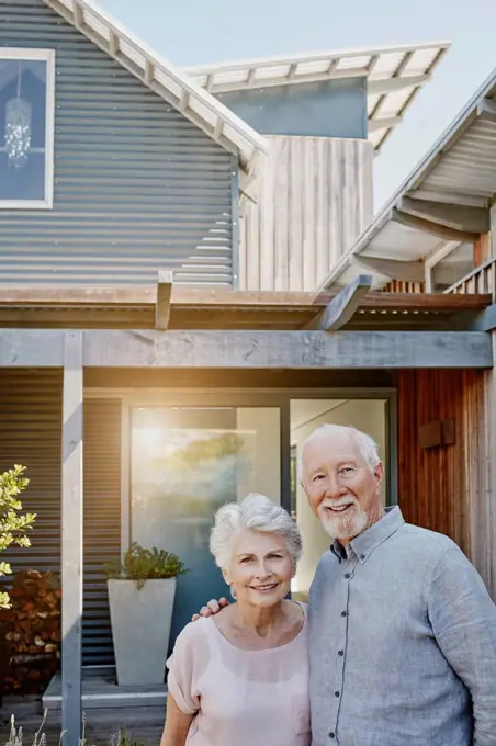 Senior couple standing in front of their house, looking confident
