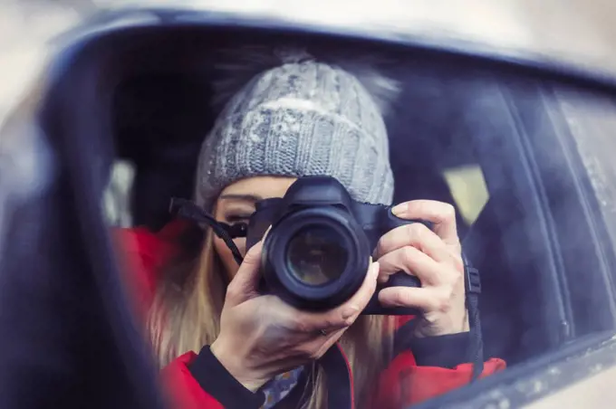 Wing mirror with mirror image of woman taking picture of herself, close-up
