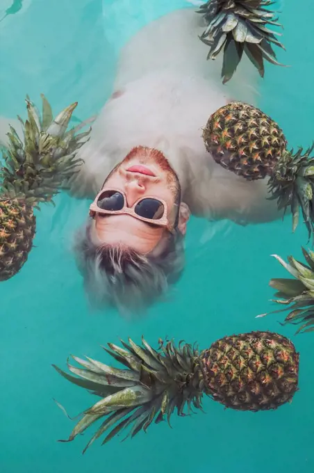 Young man in swiming pool surrounded by pineapples