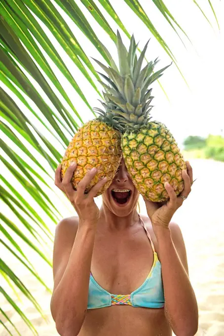 Young woman holding two pineapples at palm tree
