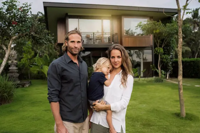 Portrait of smiling family standing in front of their design house surrounded by lush tropical garden