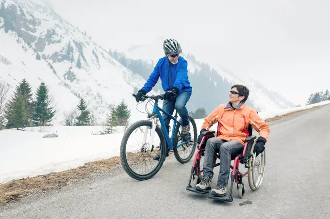Austria, Damuels, senior couple with bike and wheelchair enjoying a winter day