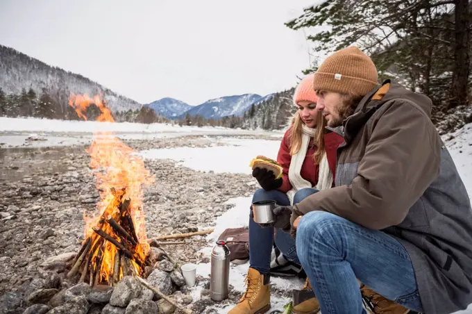 Couple on a trip in winter having a break at camp fire