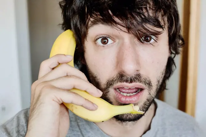Portrait of astonished young man telephoning with banana