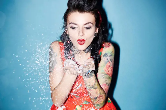 Portrait of tattooed woman blowing artificial snow