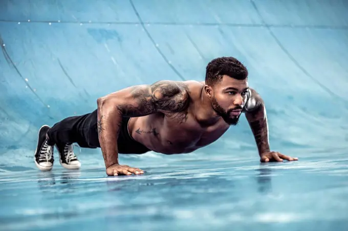 Tattooed physical athlete doing pushups on sports field