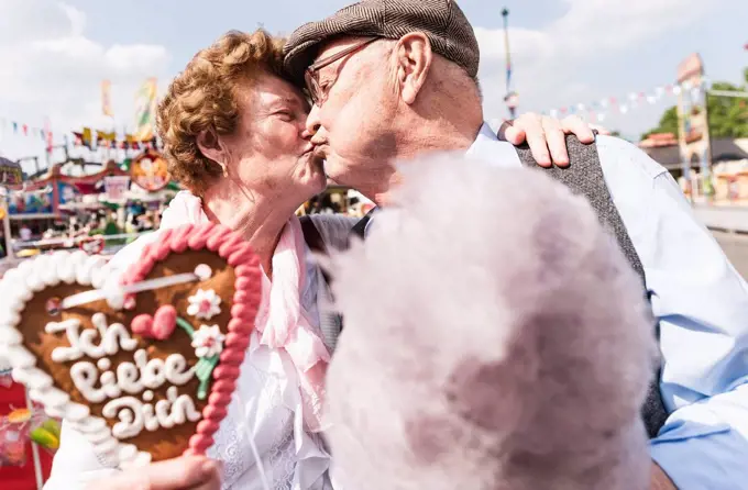 Senior couple with gingerbread heart and cotton candy kissing on fair