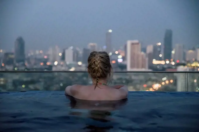 Thailand, Bangkok, back view of woman bathing in Infinity Pool looking at skyline