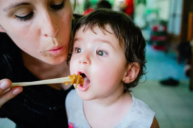 Thailand, Chiang Mai, Mother feeding her daughter with Pad Thai, using chopsticks
