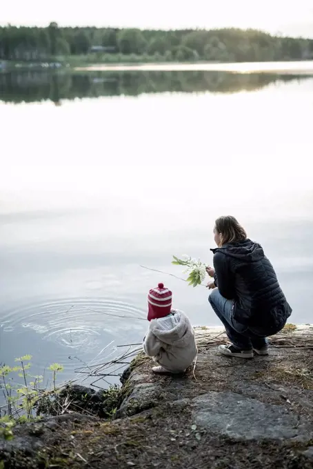 Finland, Kuopio, mother and daughter crouching at a lake