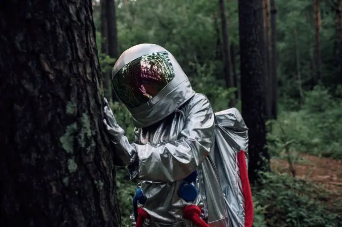 Spaceman exploring nature, examining tree trunk