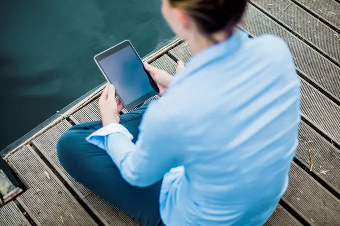 Woman sitting on jetty at a lake using tablet