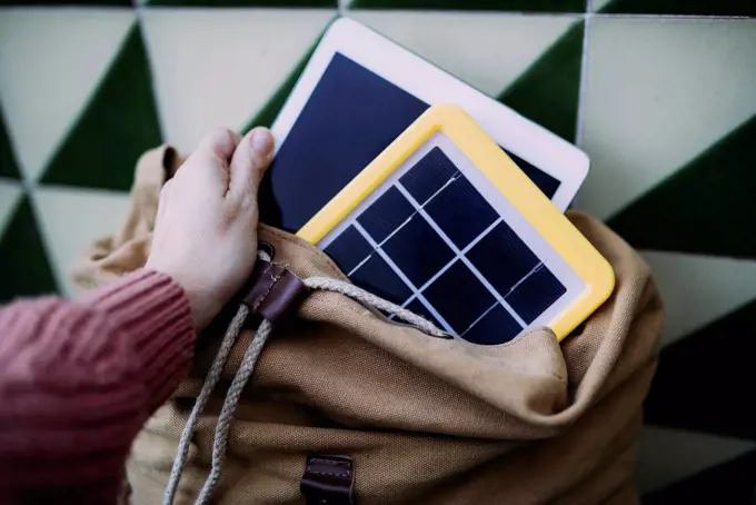 Woman putting a tablet into a backpack with a solar panel charger