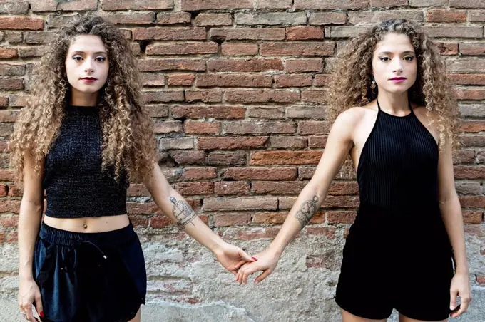 Portrait of twin sisters dressed in black holding hands