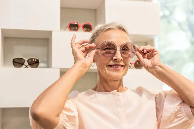 Smiling senior woman trying on sunglasses in a boutique