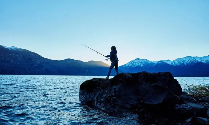 Argentina, Patagonia, Lago Futalaufquen, boy fishing in lake at dusk