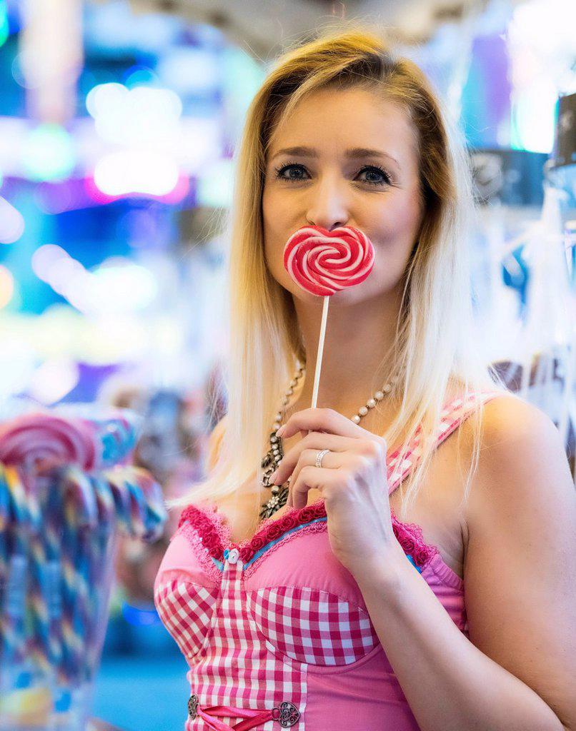 Blonde woman in pink Dirndl with lollipop in heart shape, Oktoberfest, Munich, Upper Bavaria, Bavaria, Germany