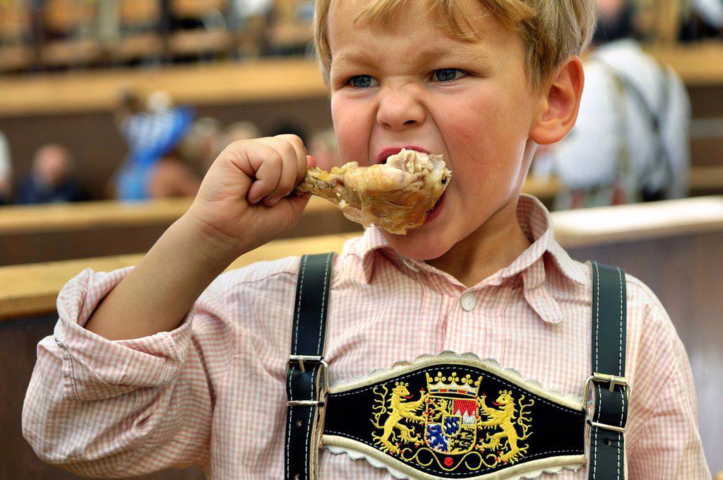 5-year old boy wearing leather pants sitting in a beer tent and eating chicken, Oktoberfest 2010, Munich, Upper Bavaria, Bavaria, Germany, Europe
