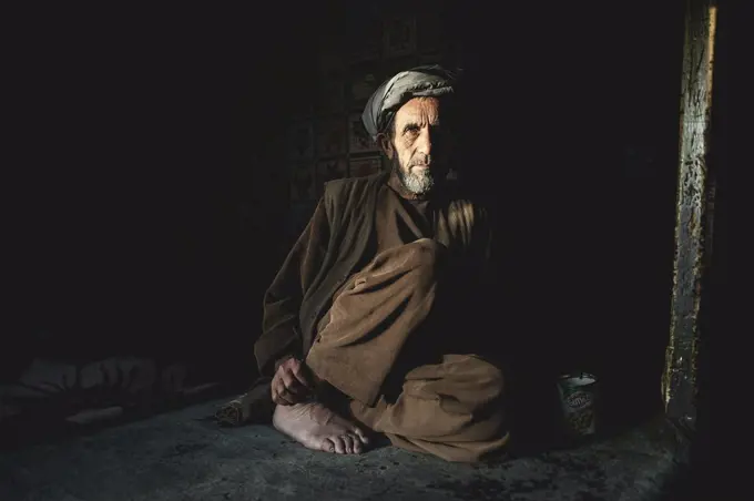 Shopkeeper sitting in the semi-darkness on the floor of his shop, Ishkashim, Afghanistan, Asia