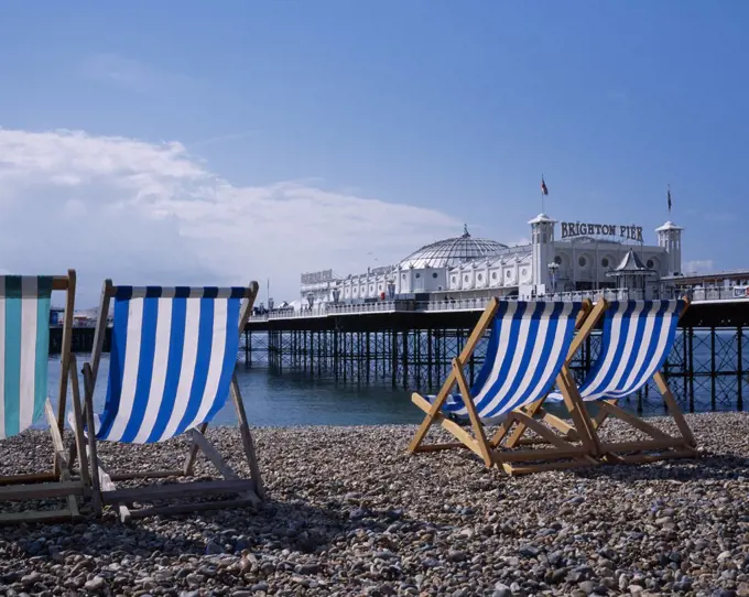 England, East Sussex, Brighton, Blue And White Striped Deckchairs On Pebble Beach Over Looking Brighton Pier.