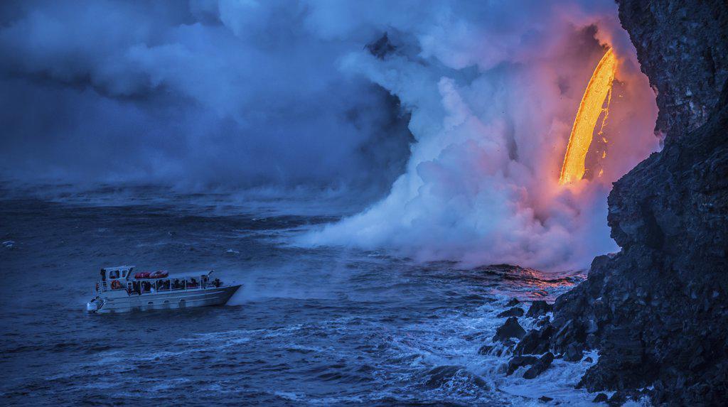 A tour boat observes lava pouring into the sea from 60 feet above as steam plumes billow up, Hawaii Volcanoes National Park, UNESCO World Heritage Site, Hawaii, United States of America, Pacific