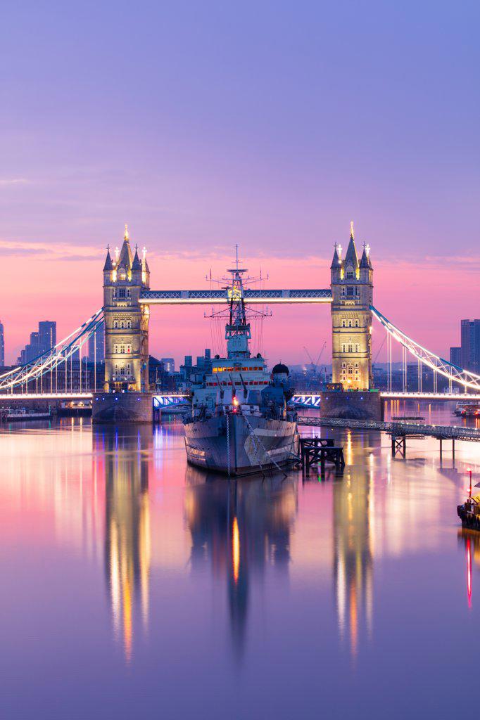 Sunrise view of HMS Belfast and Tower Bridge reflected in River Thames, with Canary Wharf in background, London, England, United Kingdom, Europe