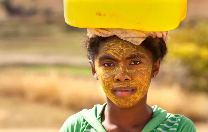 Portrait of woman carrying water, with her face painted to protect the skin from the sun, Isalo, Madagascar, Africa
