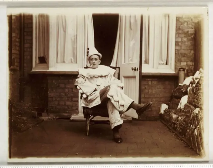 A snapshot photograph of a man dressed as a pierrot or clown, smoking a cigarette, taken by an unknown photographer in about 1930.  Originally a shoot...