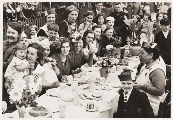 A photograph of a street party in Battersea, London, held to celebrate the Coronation of King George VI, taken by an unknown photographer in May 1937....
