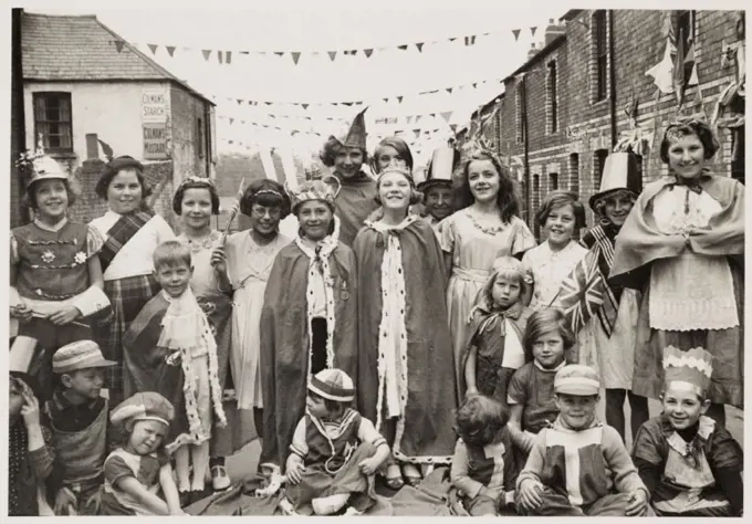 A photograph of children wearing fancy dress in Flint Street, Cardiff, Wales,taken by an unknown photographer in May 1937. The children are taking par...