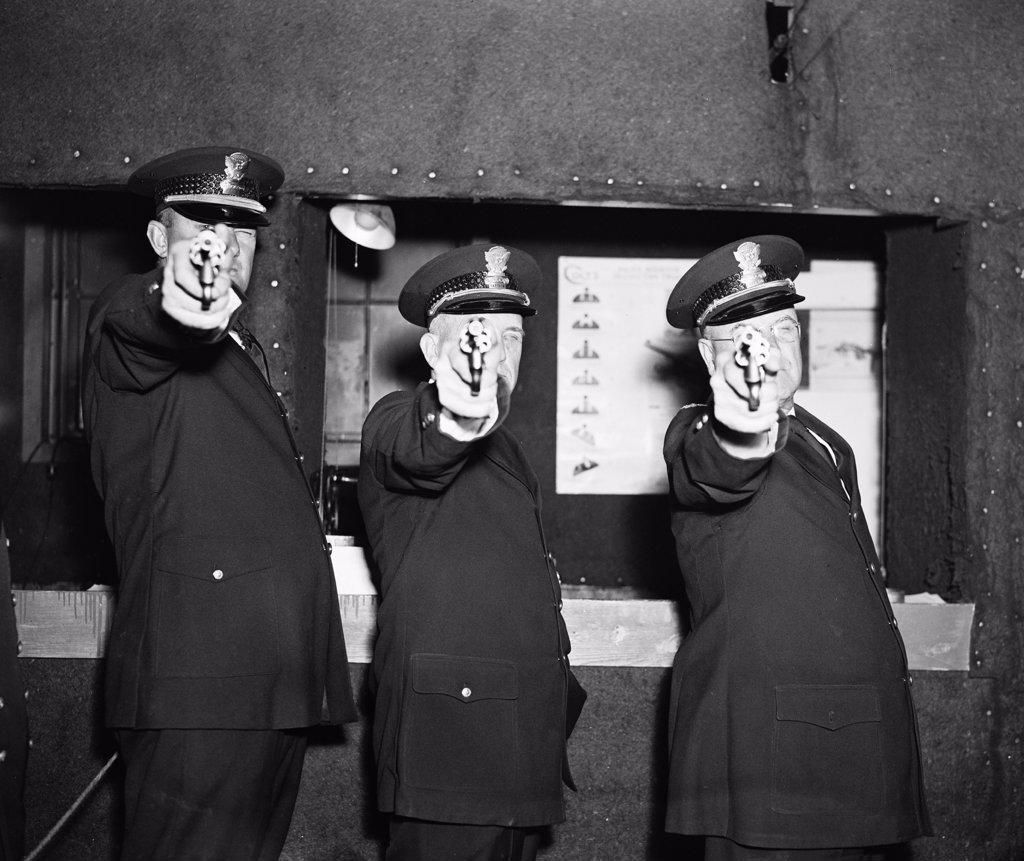 Three police officers pointing their guns (revolvers) at the photographer circa 1936.