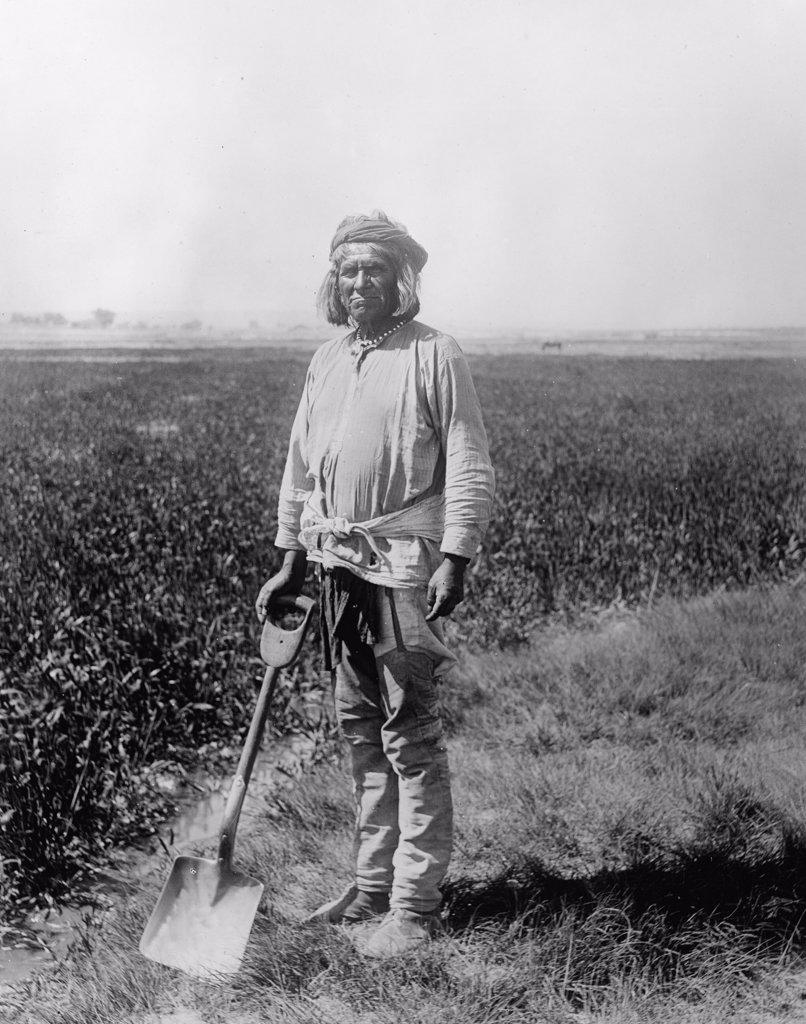 Native American man holding a shovel next to a field ca. between 1910 and 1935.