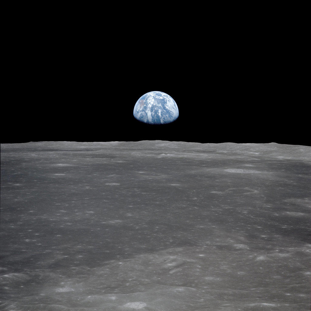 This view from the Apollo 11 spacecraft shows the Earth rising above the moon's horizon. The lunar terrain pictured is in the area of Smyth's Sea on the nearside. 
