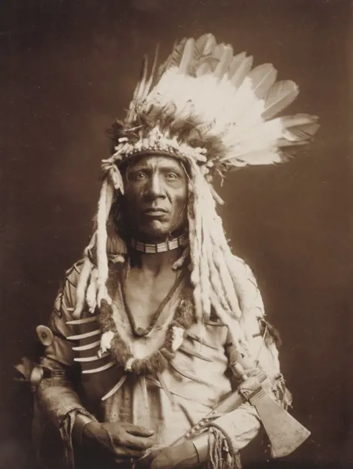 Edward S. Curtis Native American Indians - Weasel Tail, half-length portrait, facing front, holding tomahawk ca. 1900. 