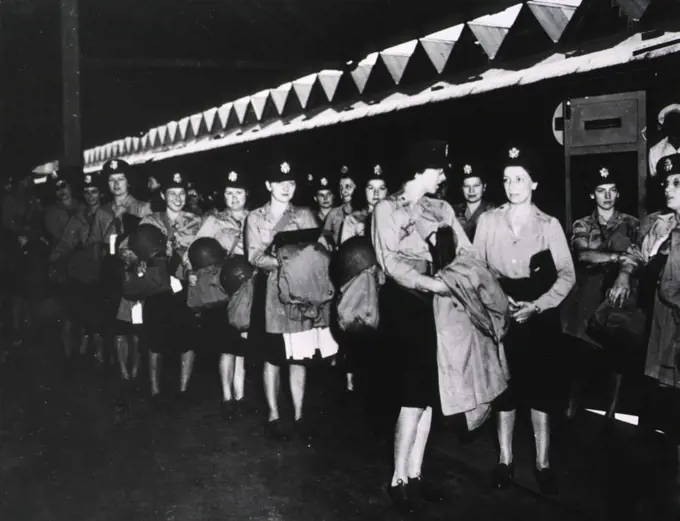 A group of female military nurses in uniform stands in rows at an unidentified location. 