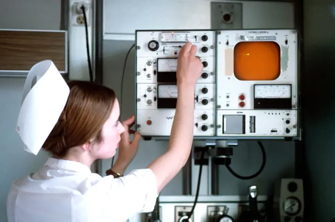 1975 - A nurse checks a monitor in a patient's room. 