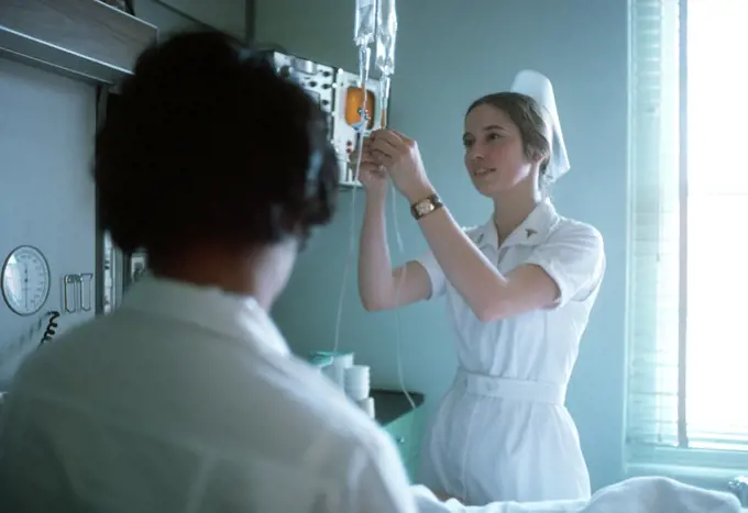 1975 - A nurse adjusts the flow of an intravenous solution. 