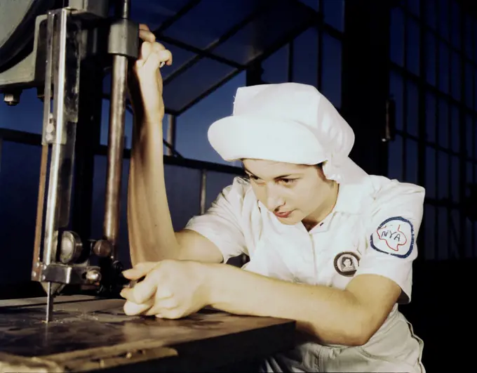 Women in white' doctor Navy planes (motors) at the Naval Air Base, Corpus Christi, Texas. Here, an NYA trainee at the base, is learning to operate a cutting machine in the Assembly and Repair Department. August 1942. 
