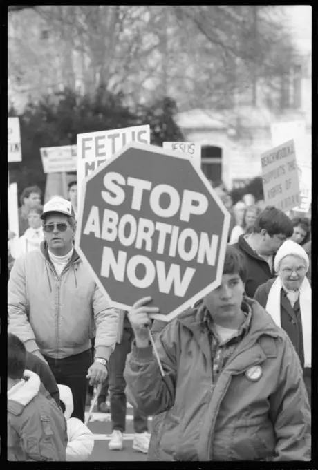 Young person holding a sign that has "Stop Abortion Now" written on it at a pro-life march, Washington, DC, 1/22/1990.