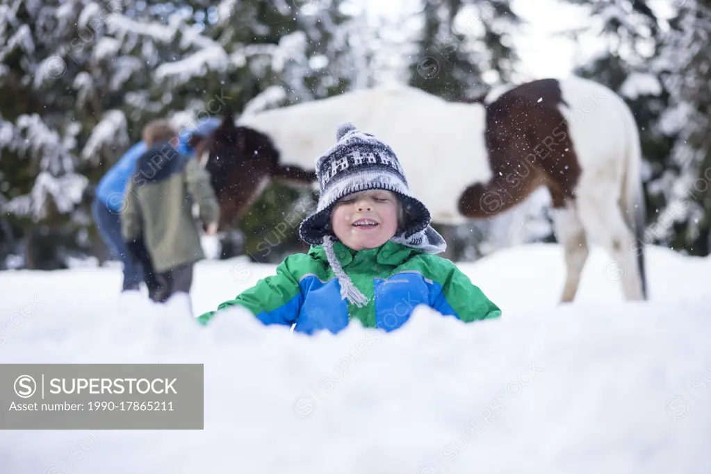 A young boy playing in the snow in front of a horse in British Columbia