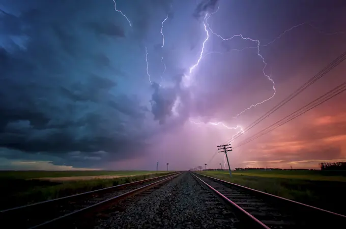 Storm with lightning flashing overhead railway crossing and train tracks at sunset near Portage la Prairie Manitoba Canada
