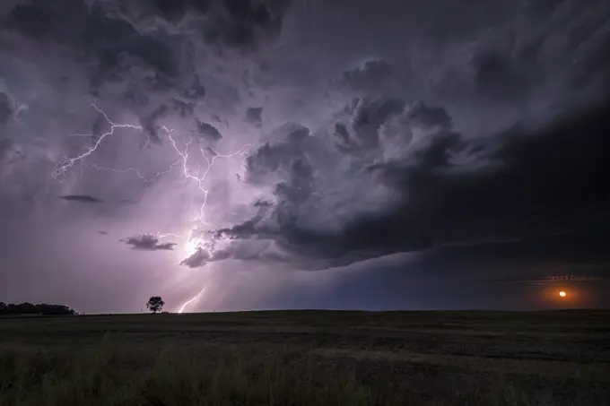 A rising moon and a storm with lightning striking over field in rural North Dakota United States