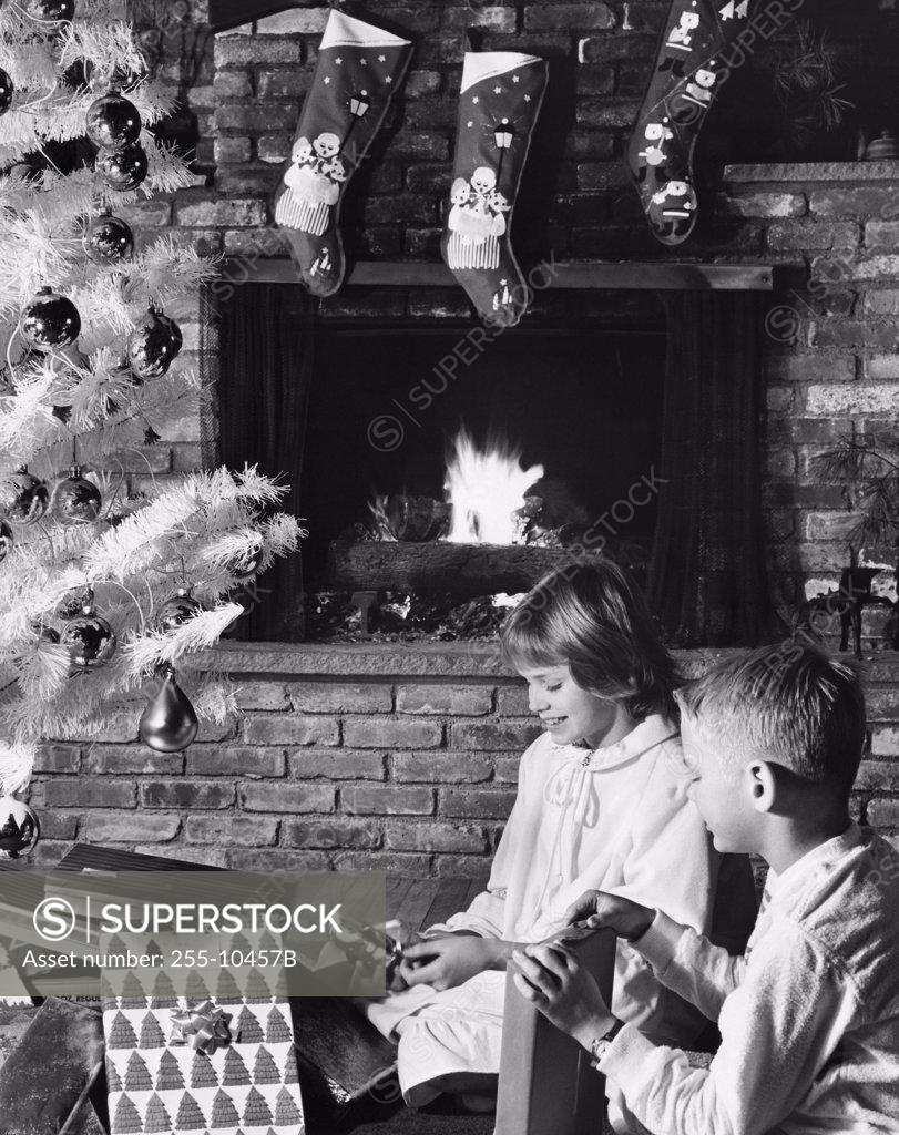 Stock Photo: 255-10457B Side profile of a girl and her brother unwrapping Christmas presents near a fireplace