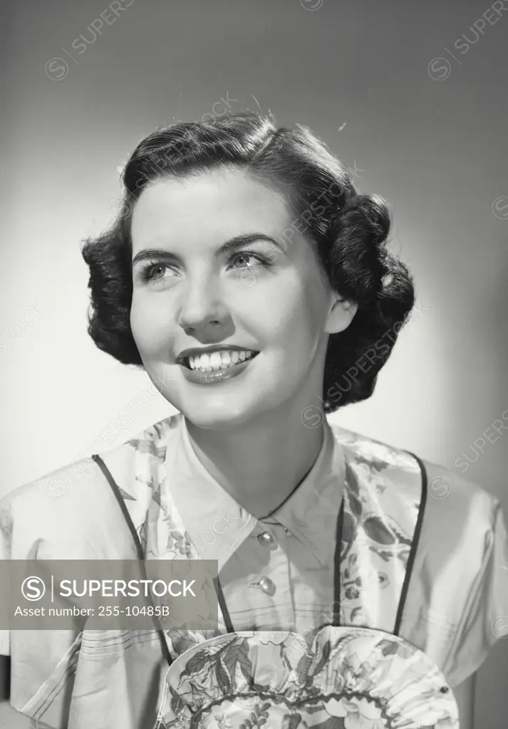 Vintage Photograph. Smiling brunette woman with curled hair wearing floral apron over blouse